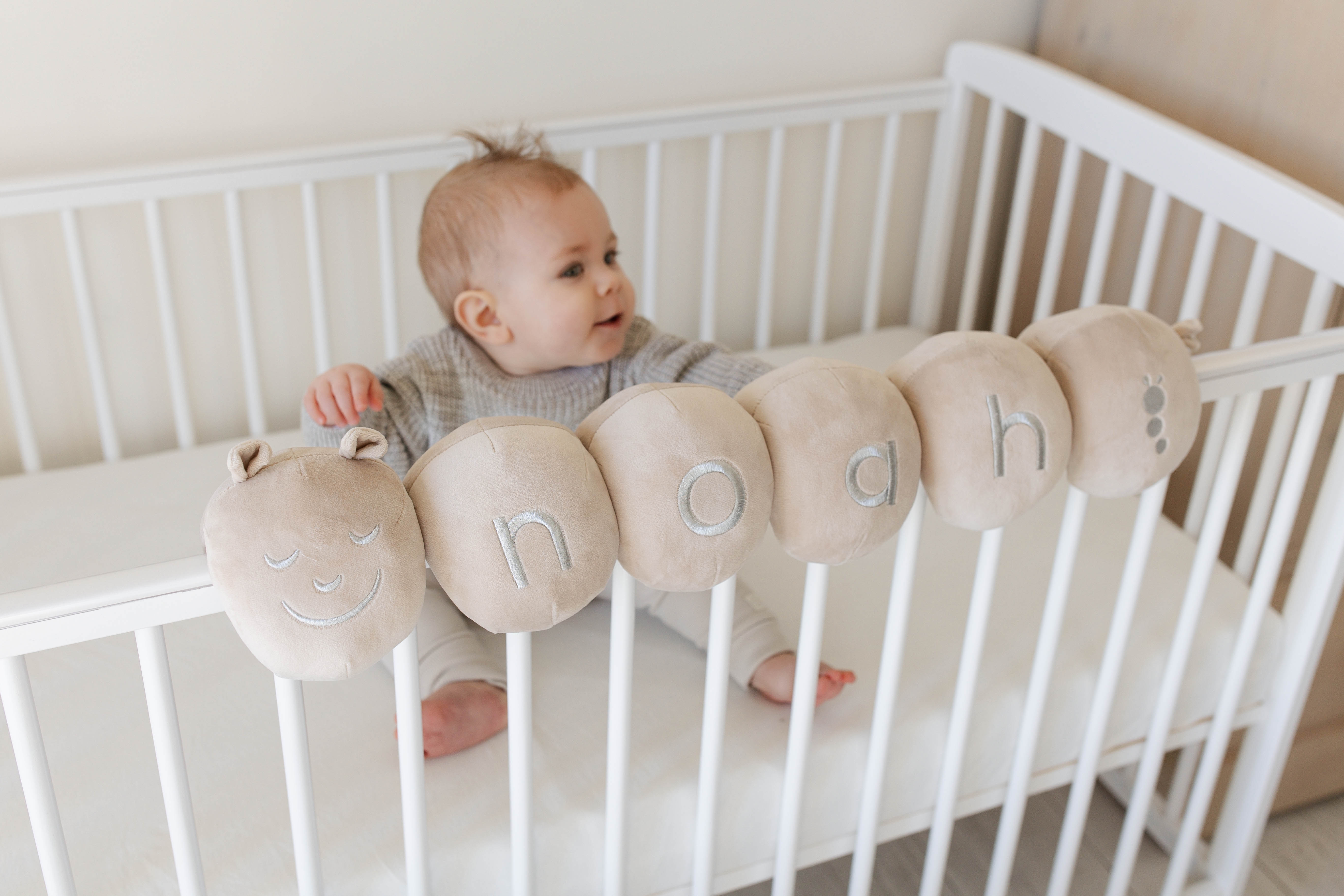 A personalised Cotterpillar fitted securely to a cot with a baby behind it